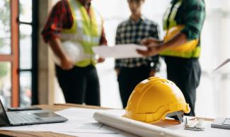 Hard hat on a desk with three people standing out of focus in the background